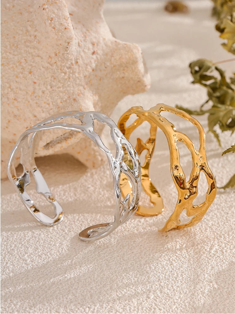 Gold and silver cuff bracelets on a textured surface with natural elements.