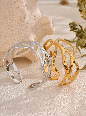 Gold and silver cuff bracelets on a textured surface with natural elements.