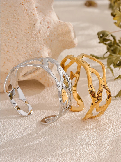 Gold and silver cuff bracelets on a textured surface with natural elements.