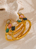 Gold bracelets with colorful gemstones on a textured beige surface