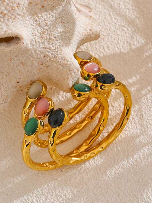 Gold bracelets with colorful gemstones on a textured beige surface