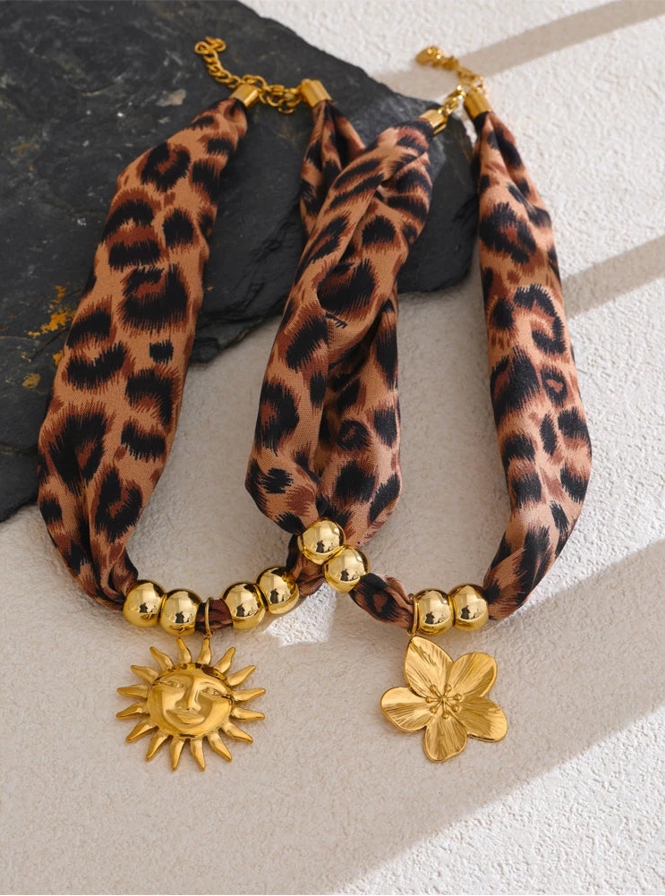 Leopard printnecklaces with gold beads and sun and flower charms on a textured surface