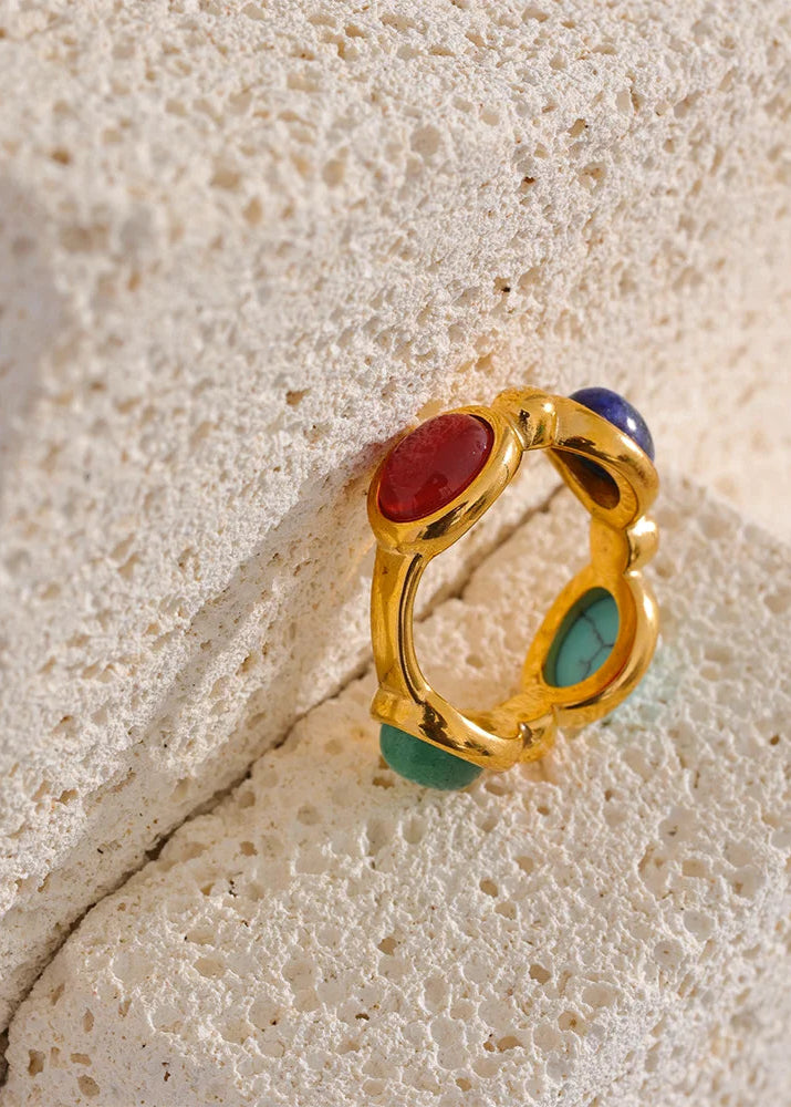 Gold ring with colored stones on a textured beige surface