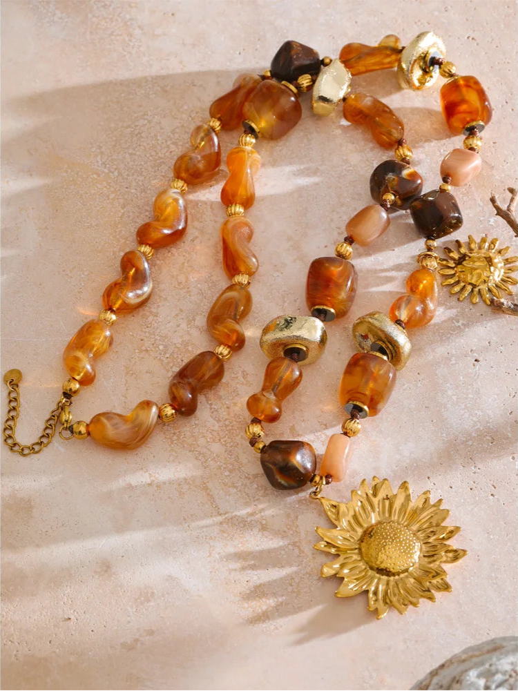 Necklace with amber beads and gold sunflower pendants on a textured surface