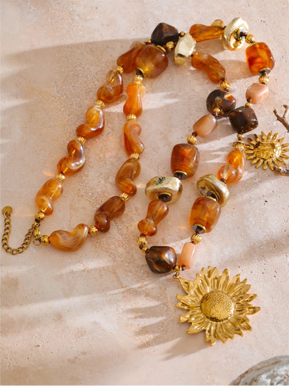 Necklace with amber beads and gold sunflower pendants on a textured surface